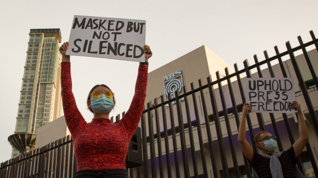 Two people holding up protest signs and wearing medical masks