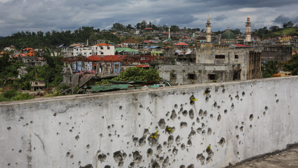 Landscape of a town, the wall in the foreground has bullet marks
