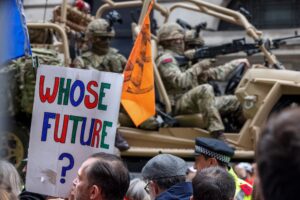 Member of Extinction Rebellion protest in front of heavily armed troops. A sign reads: 'Whose Future?' Crispin Hughes/Panos Pictures.